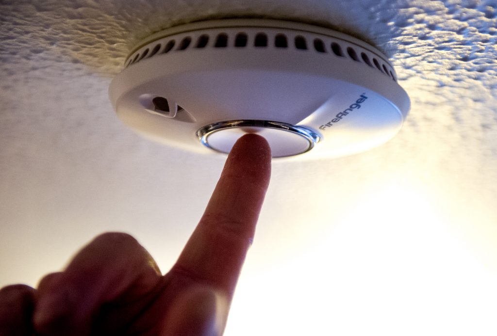 A finger reaching up to test a smoke alarm