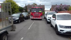 A crew in a fire engine attempting to drive down a street with heavy parking on either side