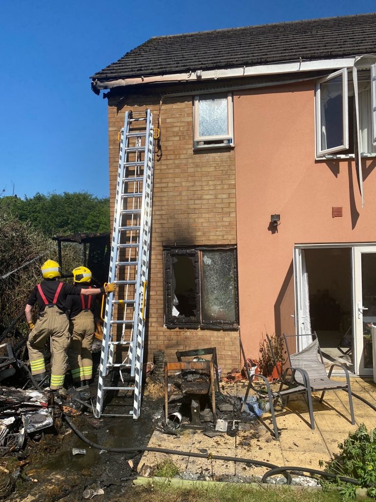 External view of domestic property badly damaged by fire with 2 firefighters and a ladder