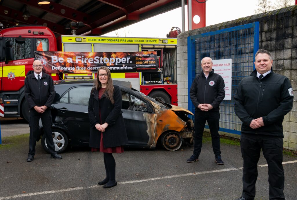 Arson Task Force, the Chief Fire Officer and the PFCC in front of a burnt out car and a FireStoppers poster