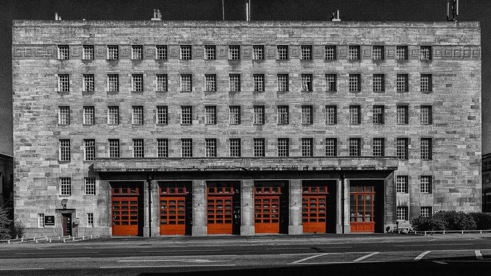 Part black and white external view of the Mounts Fire Station with red appliance bay doors