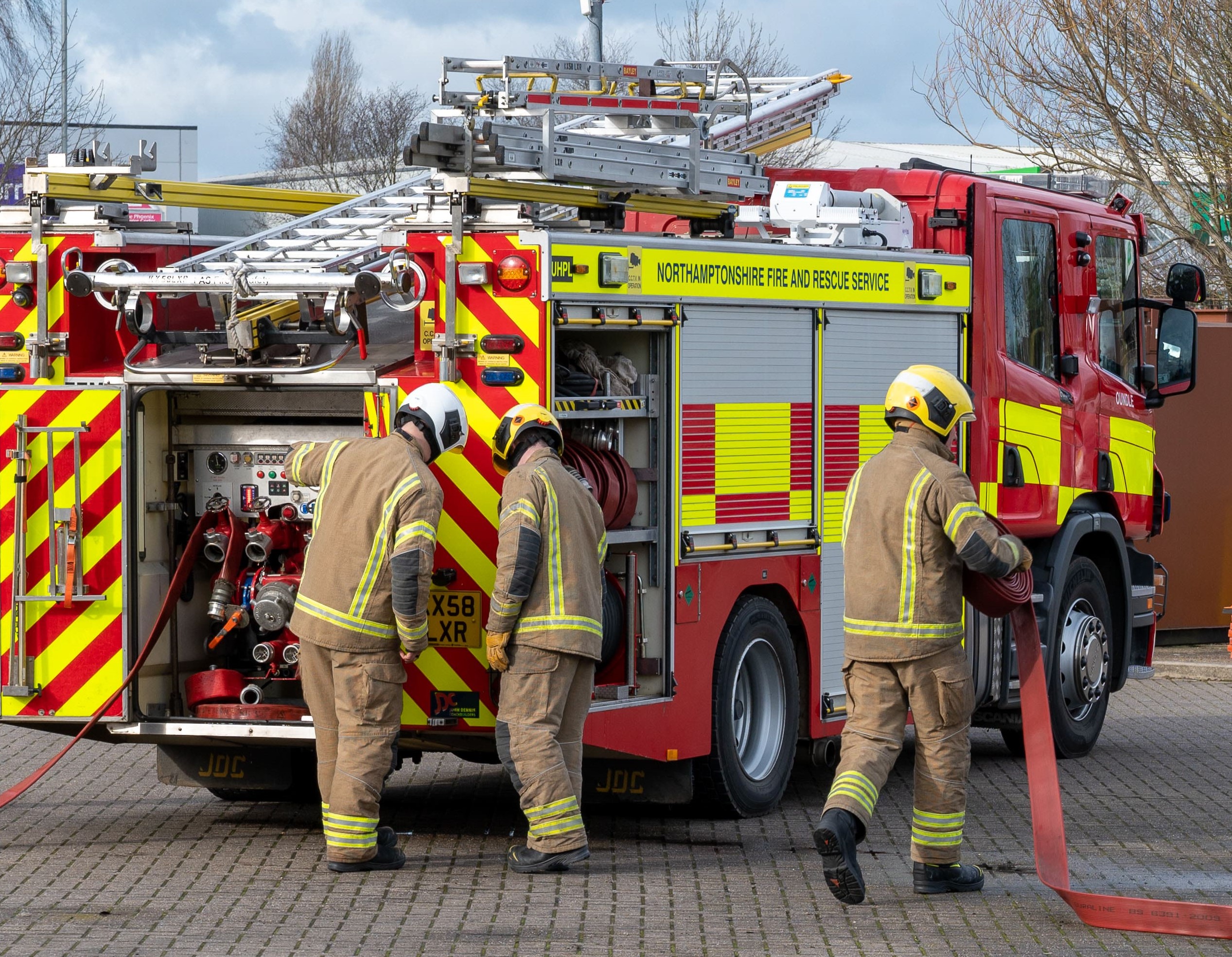 Firefighters with hose and equipment by fire appliance