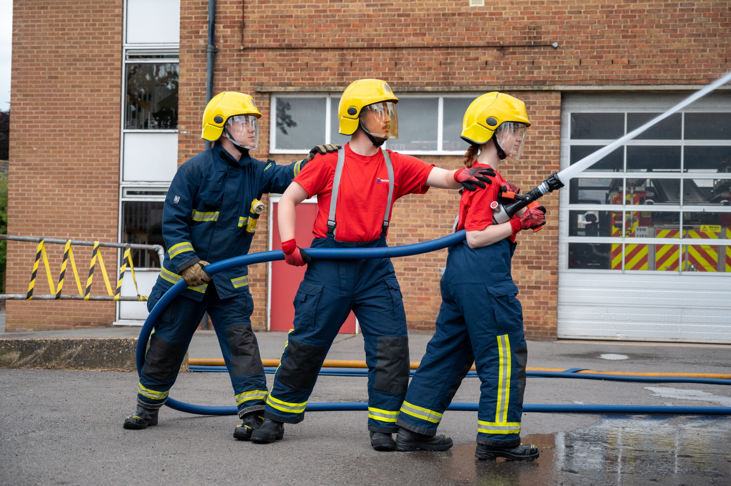 Three emergency services cadets using a firefighting hose