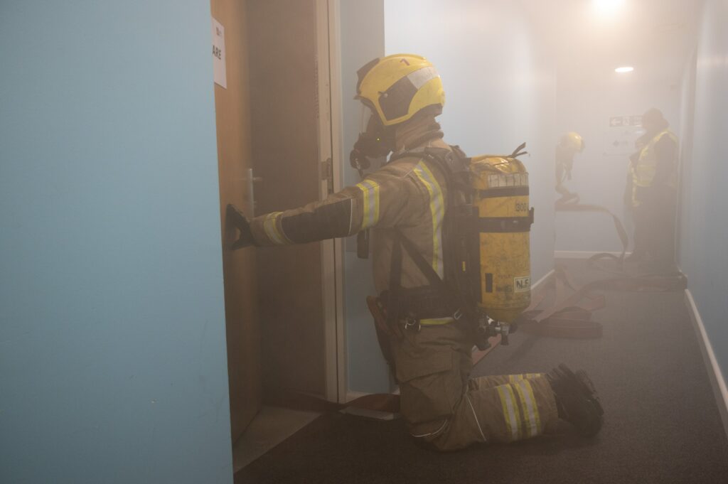 A firefighter attempts to enter a flat in a building engulfed in smoke during a training exercise