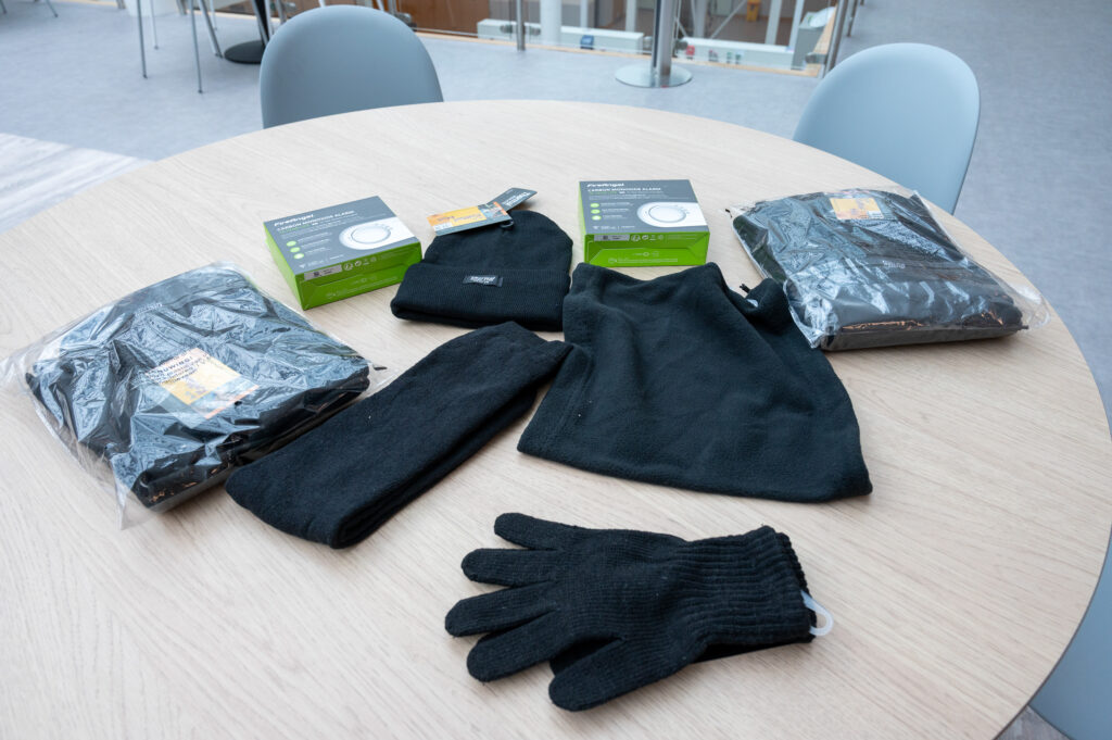 Two carbon monoxide alarms, thermal gloves, a thermal hat and snood, are pictured on a table to show what is in the Winter Warmth pack.