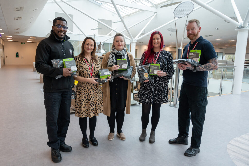 Five people hold up carbon monoxide alarms and other items which are included in the Winter Warmth packs donated by Fire Angel.