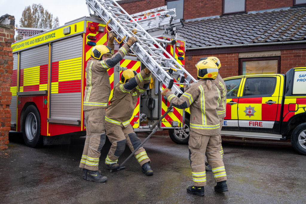 Four firefighters in full fire kit getting a ladder off a fire engine