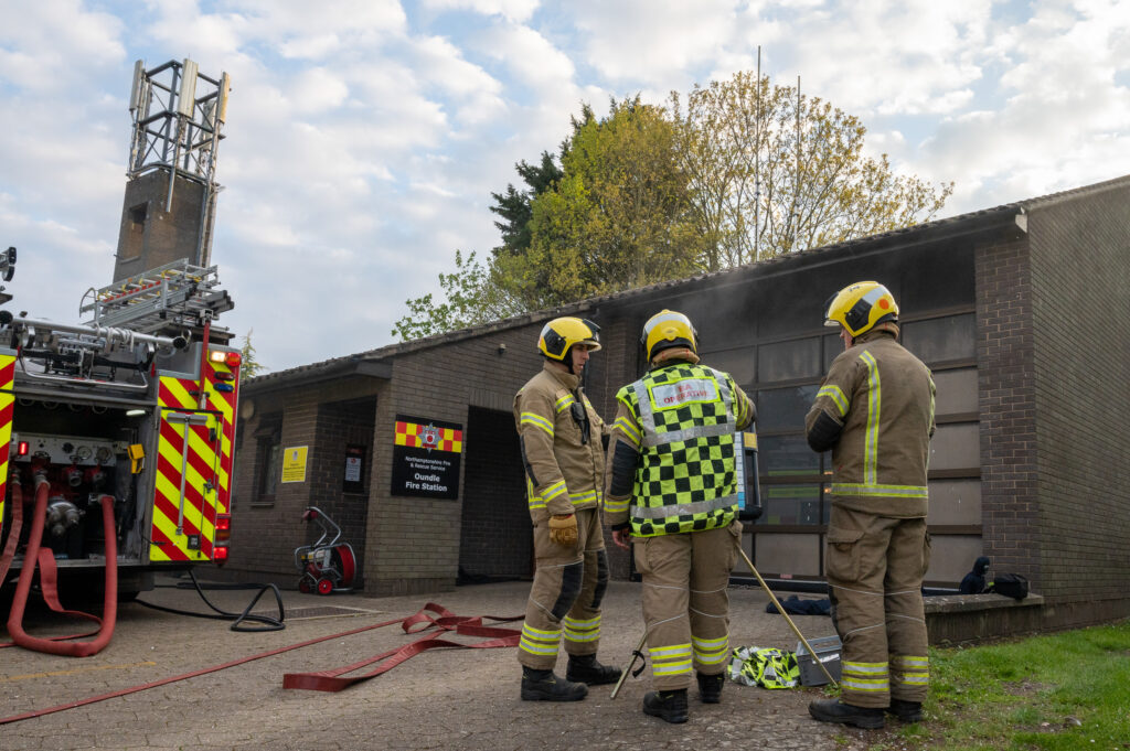 Three firefighters in fire kit monitoring a drill 