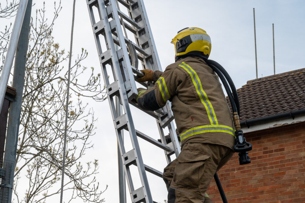 A firefighter wise hose over his shoulder, climbing a ladder