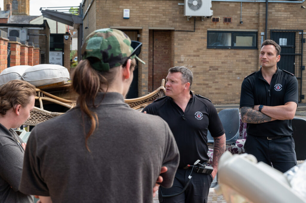 An air ambulance charity worker - wearing a green baseball cap and with his back to the camera - is given safety advice on how to avoid fly-tipped items being a target for deliberate fires. Giving the advice are Watch Manager Duncan Timbs (centre in black shirt) and firefighter Sebastien Ward (right wearing black shirt).