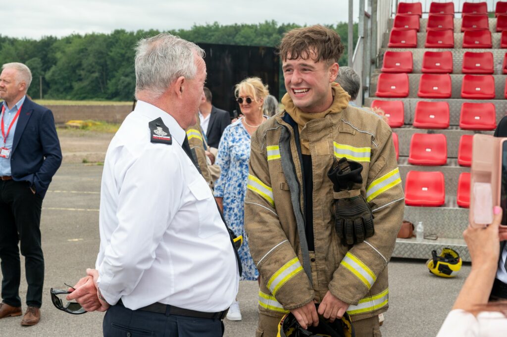Chief Fire Officer Mark Jones, in white uniform on the left, speaks with a new recruit who is pictured on the right.