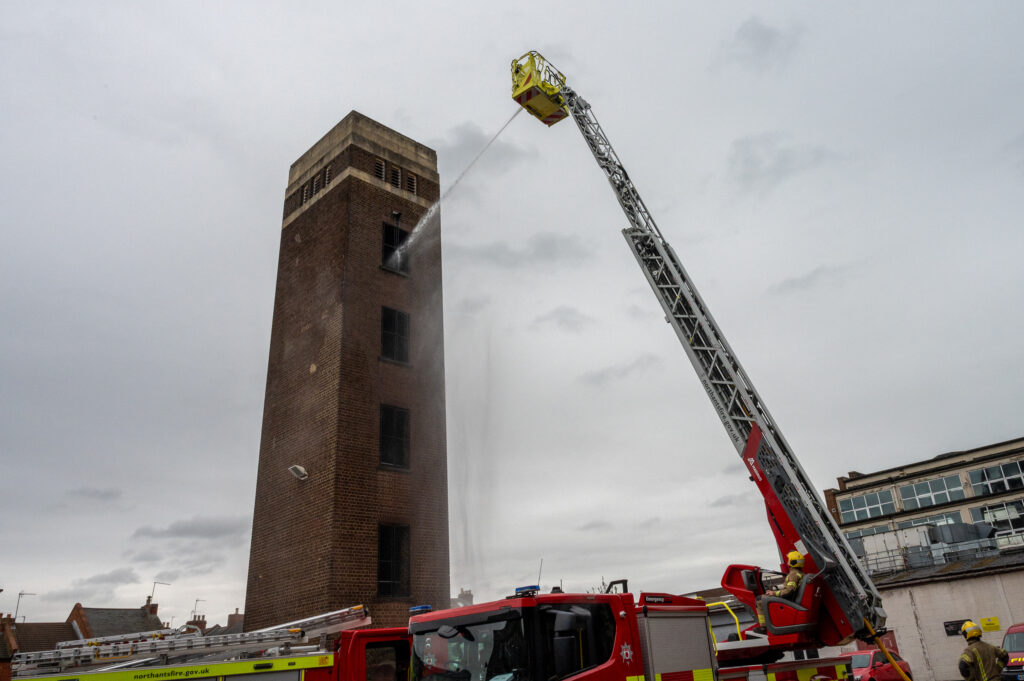The aerial appliance squirting water through the top floor of the drill tower
