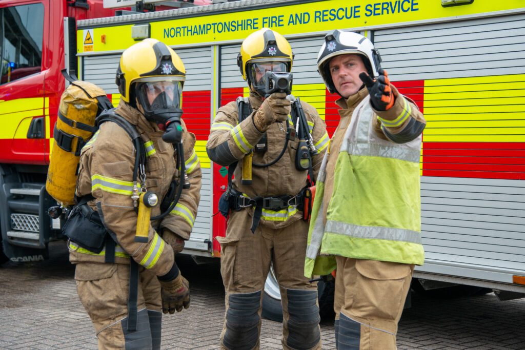Three firefighters standing in front of a fire engine discussing tactics at an incident