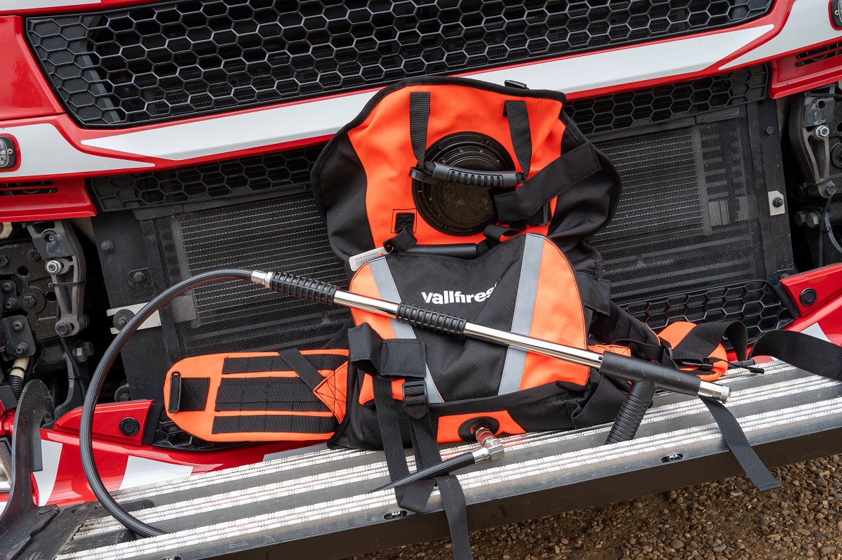 The new wildfire backpack, which is black and orange with a water pump attached, is shown in front of a fire engine