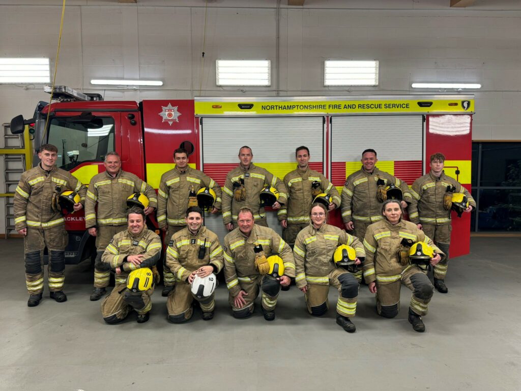 A crew of 12 firefighters stood and knelt in front of a fire engine