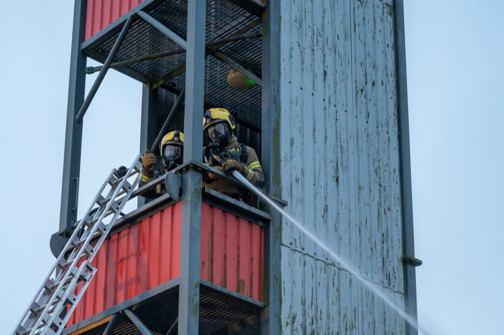 Two firefighters squirting a hose down from a tower
