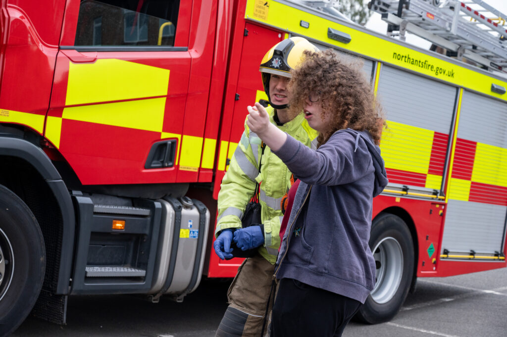 A firefighter in full kit talking to a member of the GAINN project in front of a fire engine