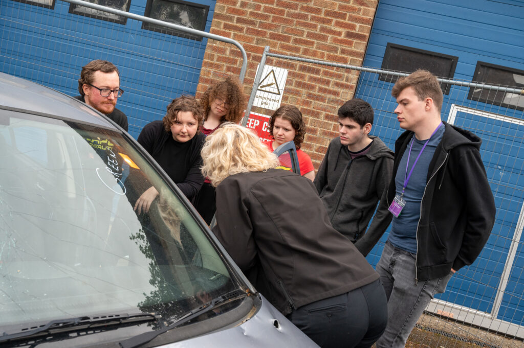 A group of students gathered around a car, speaking to a member of fire staff