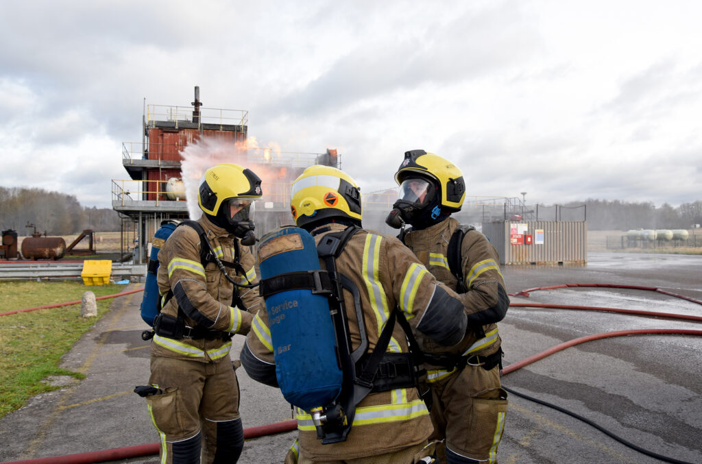 Three firefighters ensuring all of their kit is donned correctly.