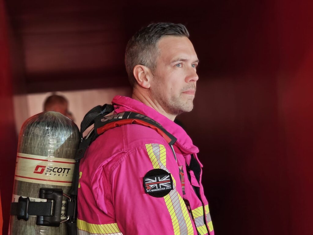 Dean Keeber wearing a pink firefighter tunic, with breathing apparatus on his back.