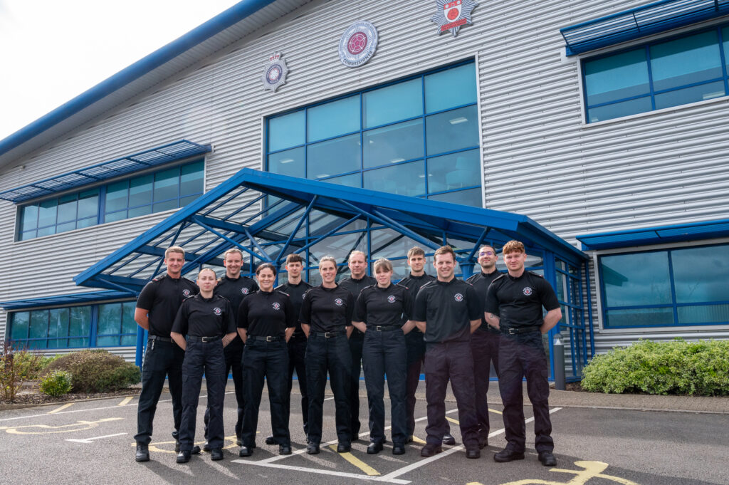 Twelve new firefighters in all black uniform stood outside fires service HQ