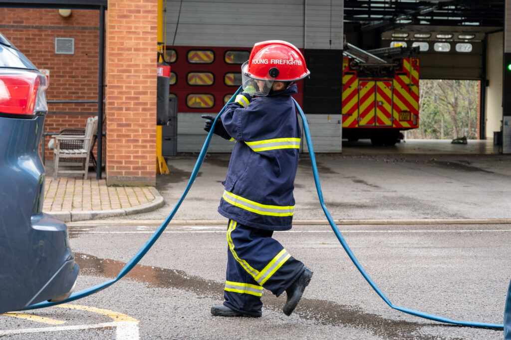 A young person in fire kit carrying a fire hose