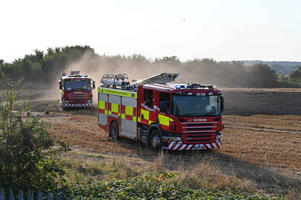 Two fire engines with blue lights on drive through a field