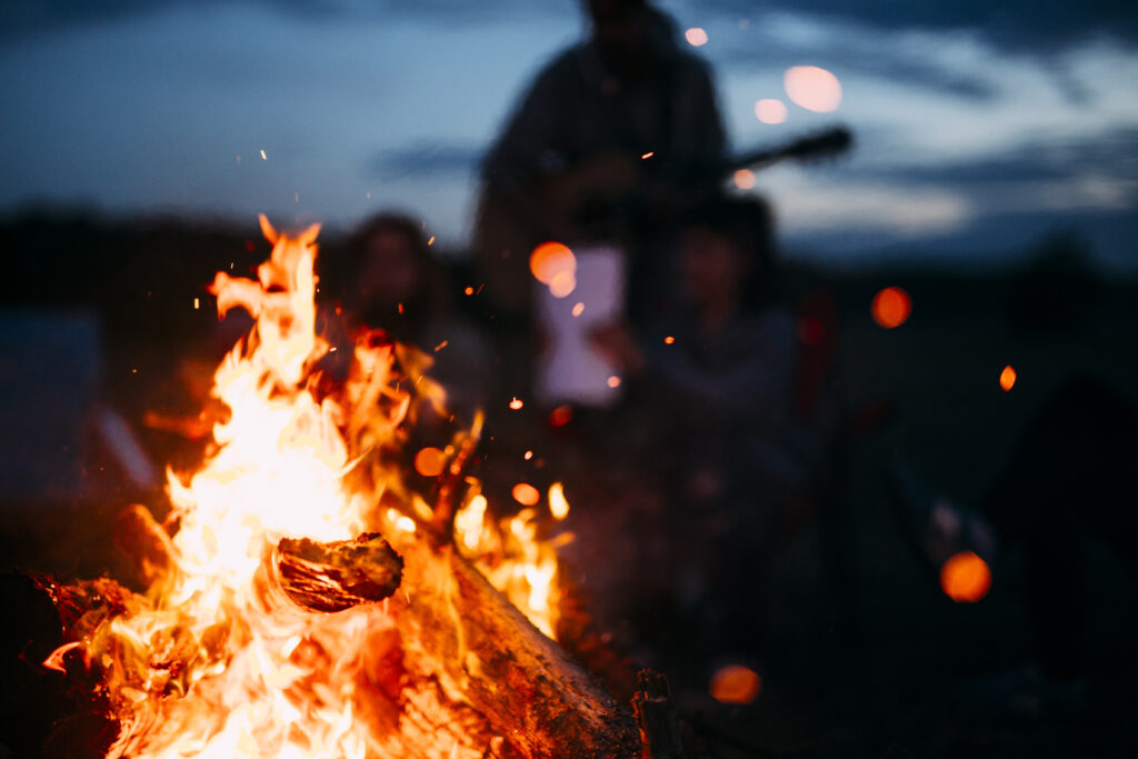 An atmospheric bonfire image shows silhouttes in the background with a campfire in the foreground.