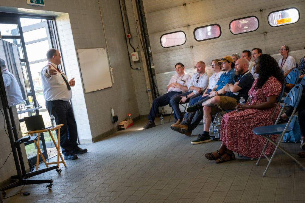 A group of local authority staff in a fire station bay listening to a presentation