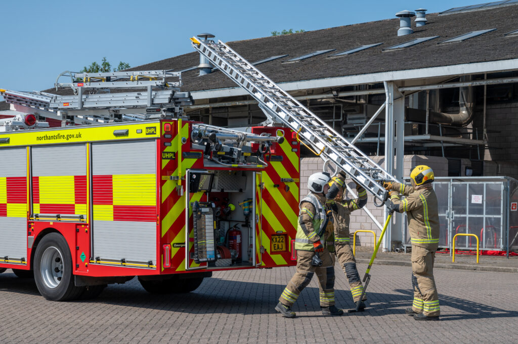Three firefighters getting a ladder off a fire engine